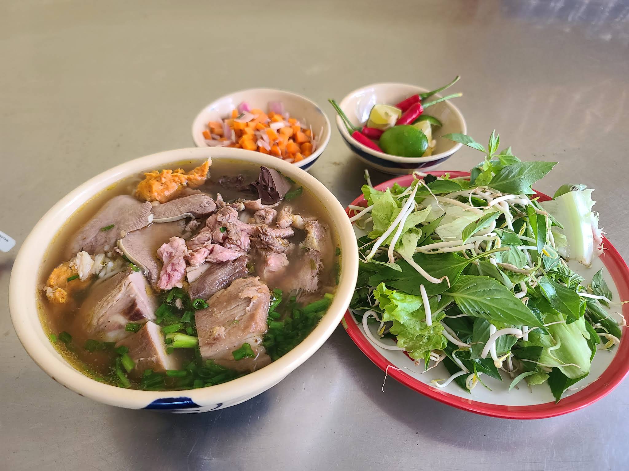 Traditional Bun Bo Hue served with fresh herb plate, bean sprouts, lime, chili, and homemade condiments at Co My restaurant Da Nang