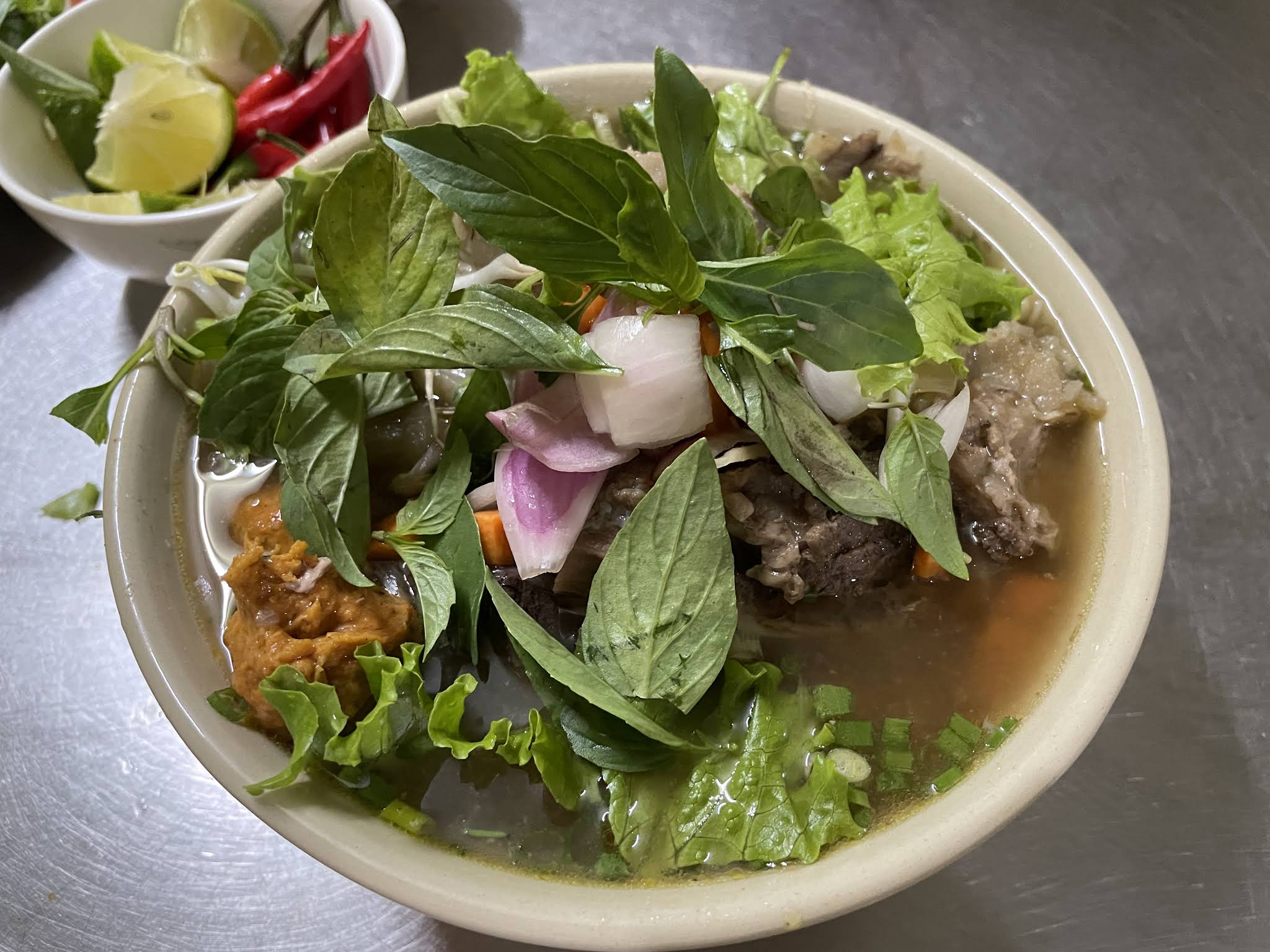 Bun Bo Hue bowl topped with fresh Thai basil, red onion, bean sprouts, and lettuce at Bun Bo Hue Co My Da Nang