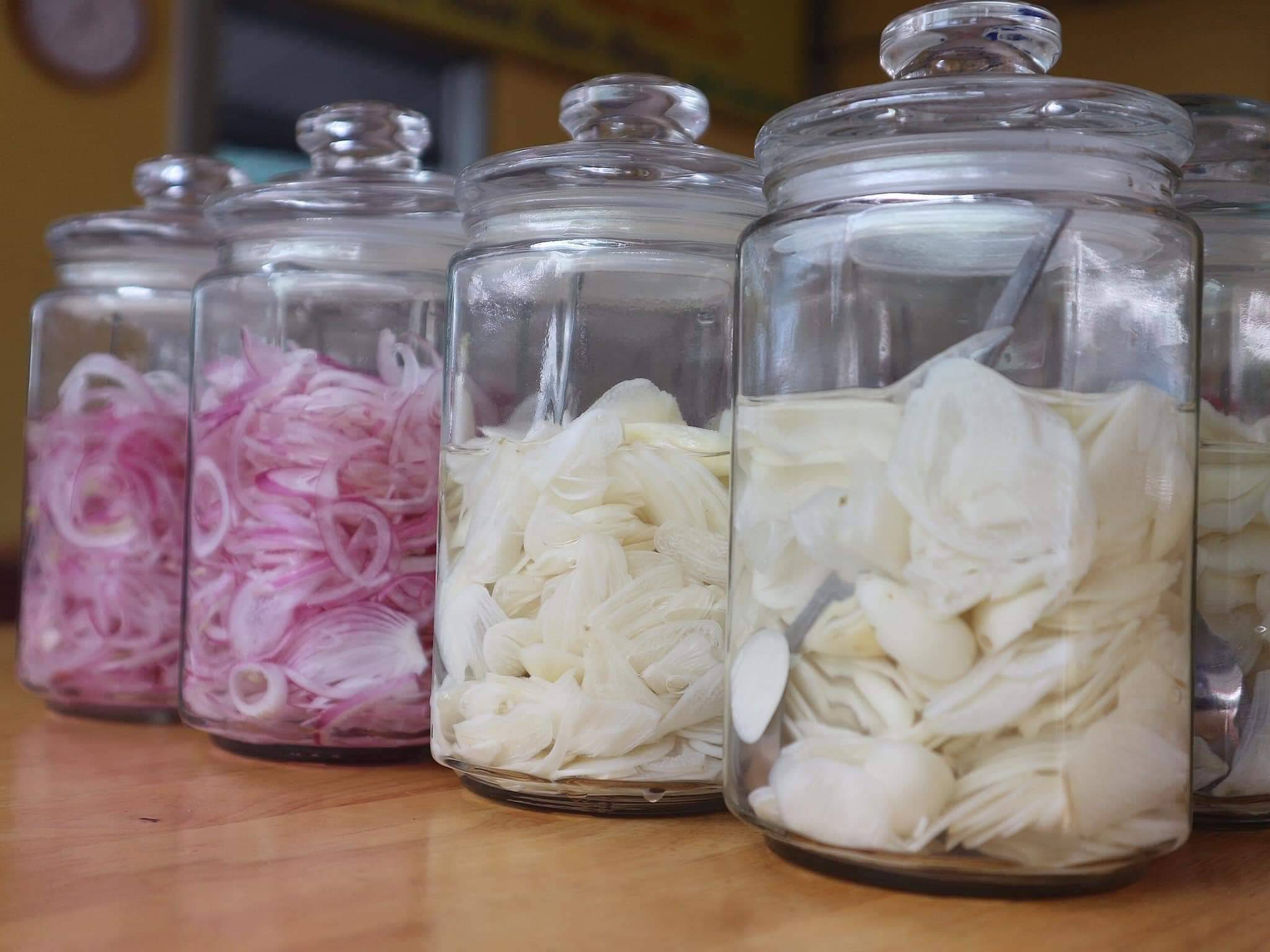 Homemade pickled red onions and garlic condiments in glass jars at Bun Bo Hue Co My Da Nang